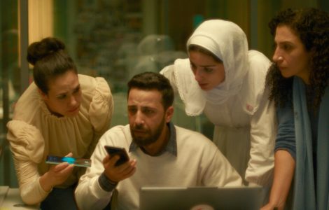 Four people gather closely around a laptop and smartphone in a softly lit office.